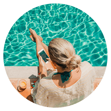 Woman relaxing by a pool, checking messages on her smartphone, enjoying a refreshing drink.