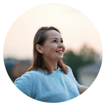 Smiling woman in a blue sweater enjoying a serene outdoor moment during sunset.