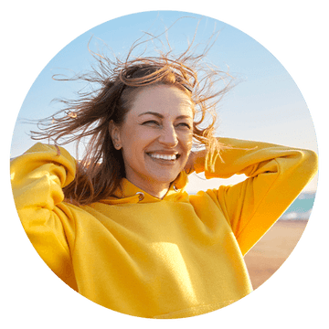 Smiling woman in a yellow hoodie enjoying a sunny day at the beach, showcasing happiness and freedom.