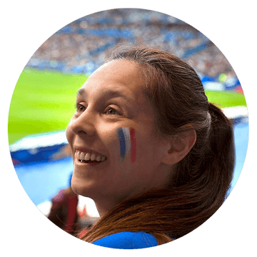 Smiling fan with a French flag face paint enjoying a soccer match in a stadium.