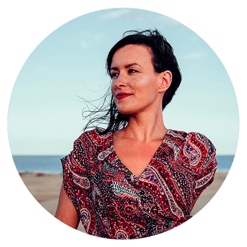 Woman in a colorful dress smiling against a beach background, showcasing confidence and beauty. Client testimonial image.