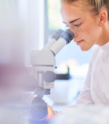 Young scientist observing specimen through a microscope in a laboratory setting.