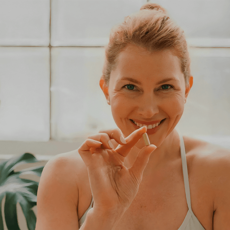 Woman smiling while holding a supplement capsule, promoting a healthy lifestyle with Harmonie Daily.