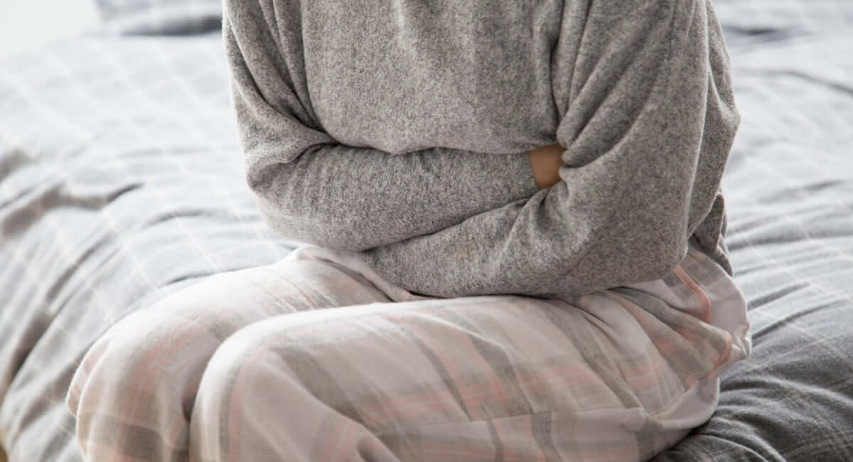 Femme assise sur un lit tenant son ventre, représentant la constipation pendant la ménopause.